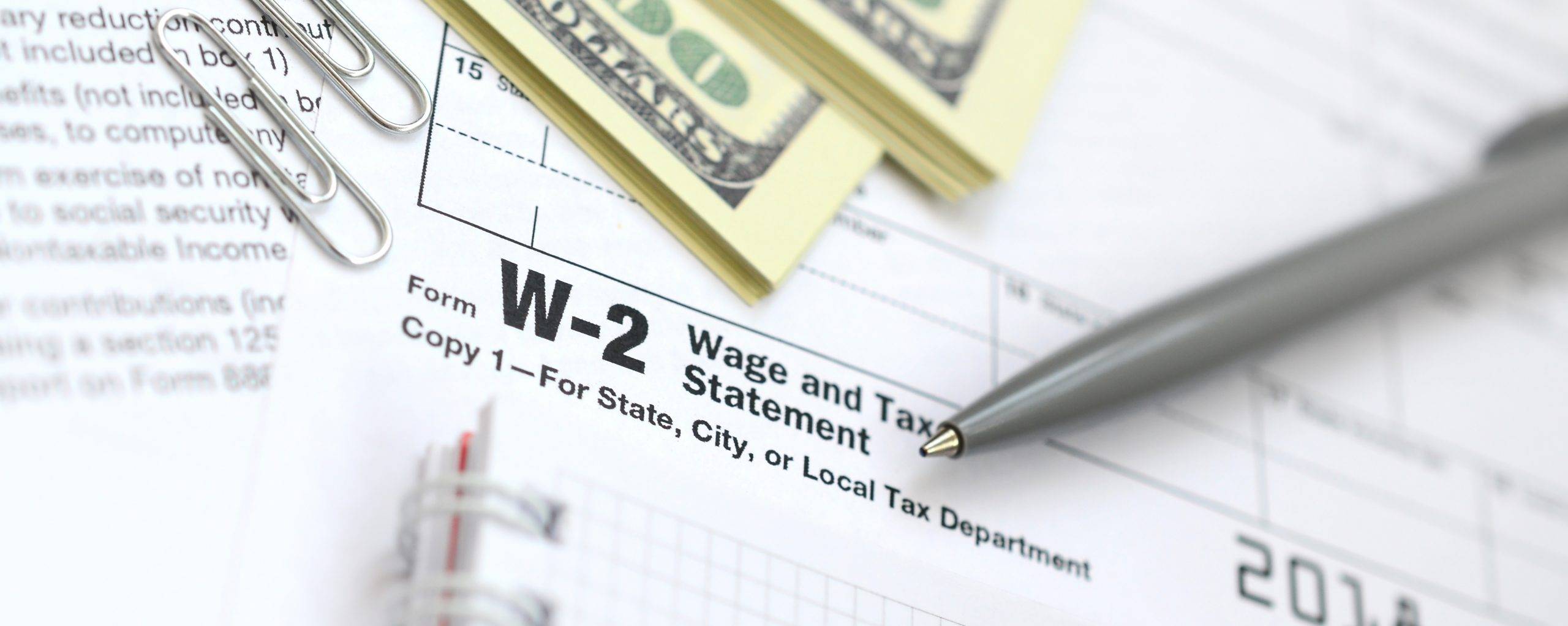 The pen, notebook and dollar bills is lies on the tax form W-2 W